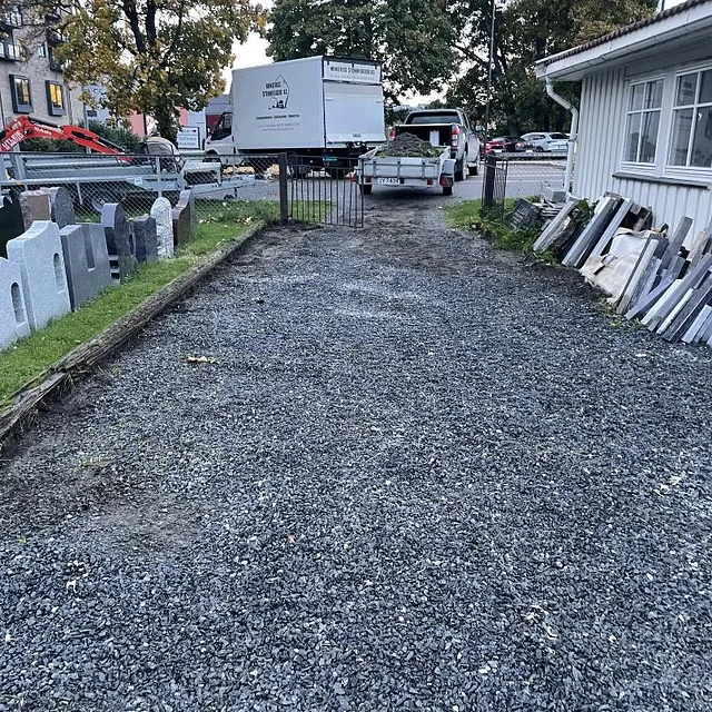 En smal innkjørsel dekket med grus som fører opp mot hus og hage.