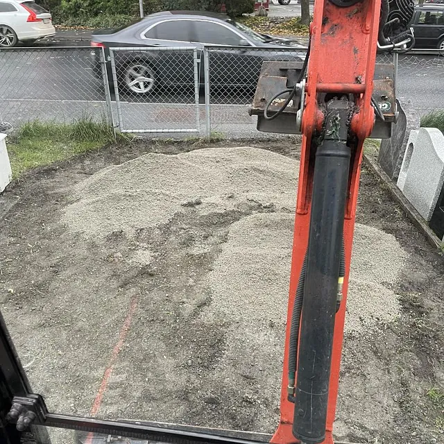 Bilde tatt fra førersetet på en gravemaskin under arbeid på en gårdsplass.