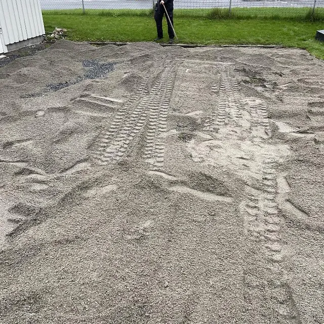 Planert sandflate på en gårdsplass med et hvitt bolighus i bakgrunnen.